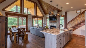 A spacious kitchen with a large island, wooden beams, and a stone fireplace.