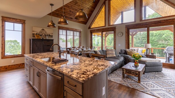 A spacious kitchen with a large island, wooden ceiling beams, and large windows offering views of the outdoors.