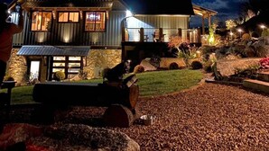A large, two-story house with a stone foundation and a metal roof, illuminated by exterior lights.