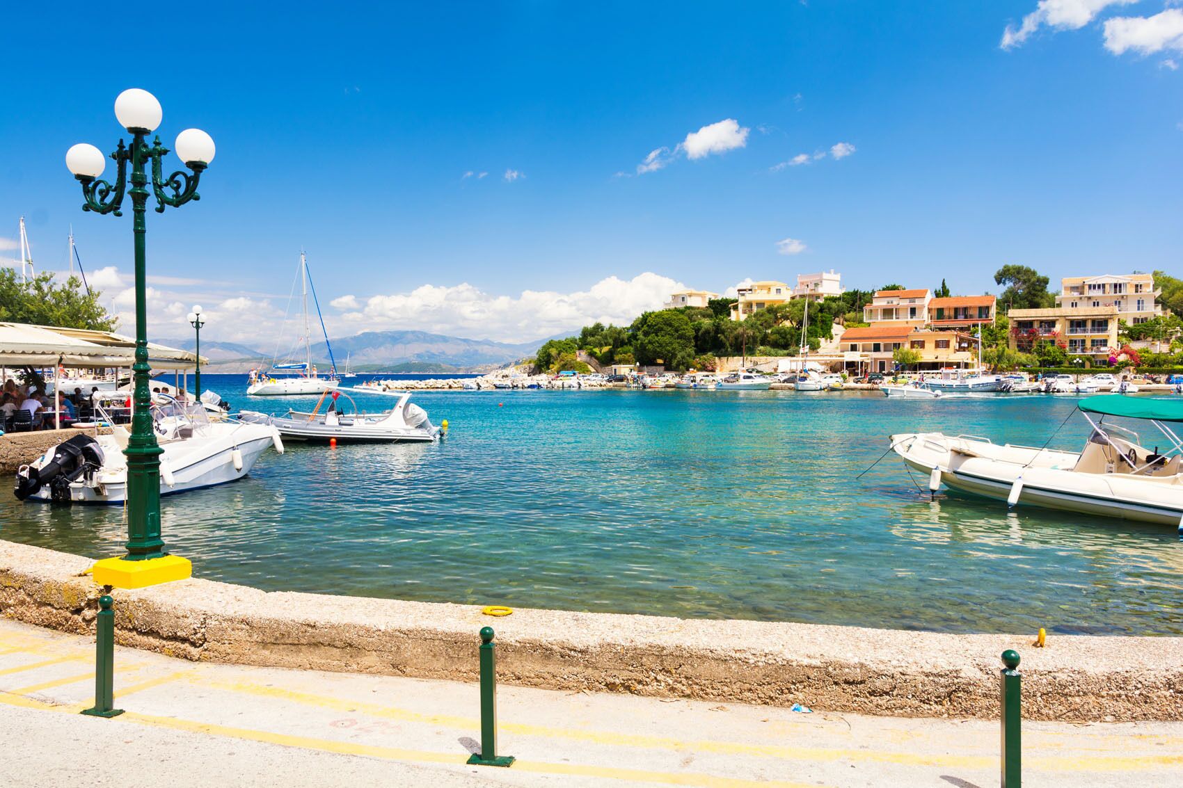 A marina with boats docked, a green street lamp, and buildings in the background.