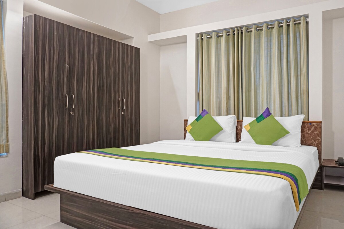 A hotel room with a large bed, a wardrobe, a nightstand, and a curtain.