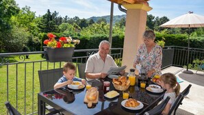 A family dining outdoors with a table set for breakfast, surrounded by greenery and a scenic view. - GÎte Les Cerisiers, 3 stars (Ailhon)
