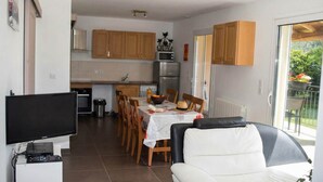 A modern kitchen with wooden cabinets, a dining area with a table set for four, and a living area with a flat-screen TV and a sofa. - GÎte Les Cerisiers, 3 stars (Ailhon)