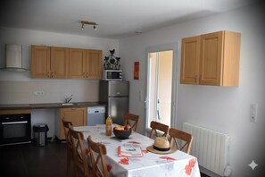 Eine Küche mit Holzausstattung, einer Mikrowelle und einem Kühlschrank. Ein Esstisch mit Stühlen und einem Hut darauf.