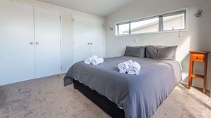 A bedroom with a large bed, a wardrobe, a window, and a bedside table. - Central Oasis - Garage & Courtyard, Sleeps 6 (Rotorua)