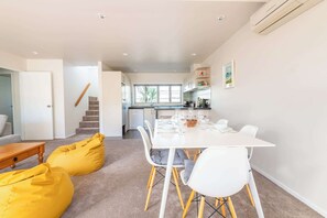 A modern kitchen with white cabinets, a dining area with a white table and chairs, and a staircase leading to another level.