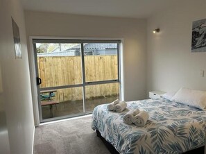 A bedroom with a bed, a window, and a door leading to a patio.