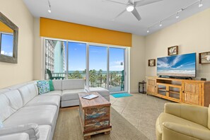 Relax in this stylish living room with a large sofa, coffee table, and armchair, plus a TV and sliding glass door to a balcony with a palm tree view.