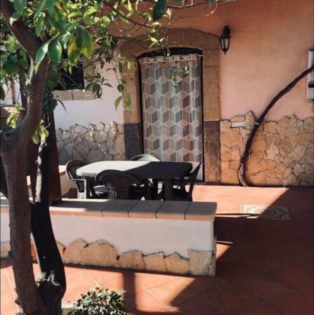 An outdoor patio with a table and chairs, a stone wall, and a door with a geometric pattern.