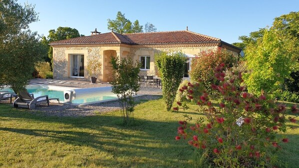 A stone house with a tiled roof, a swimming pool, and outdoor seating.