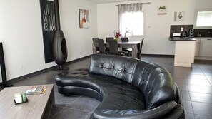 A modern living room with a black leather sofa, a dining area with a table and chairs, and a kitchen area with a countertop and appliances.