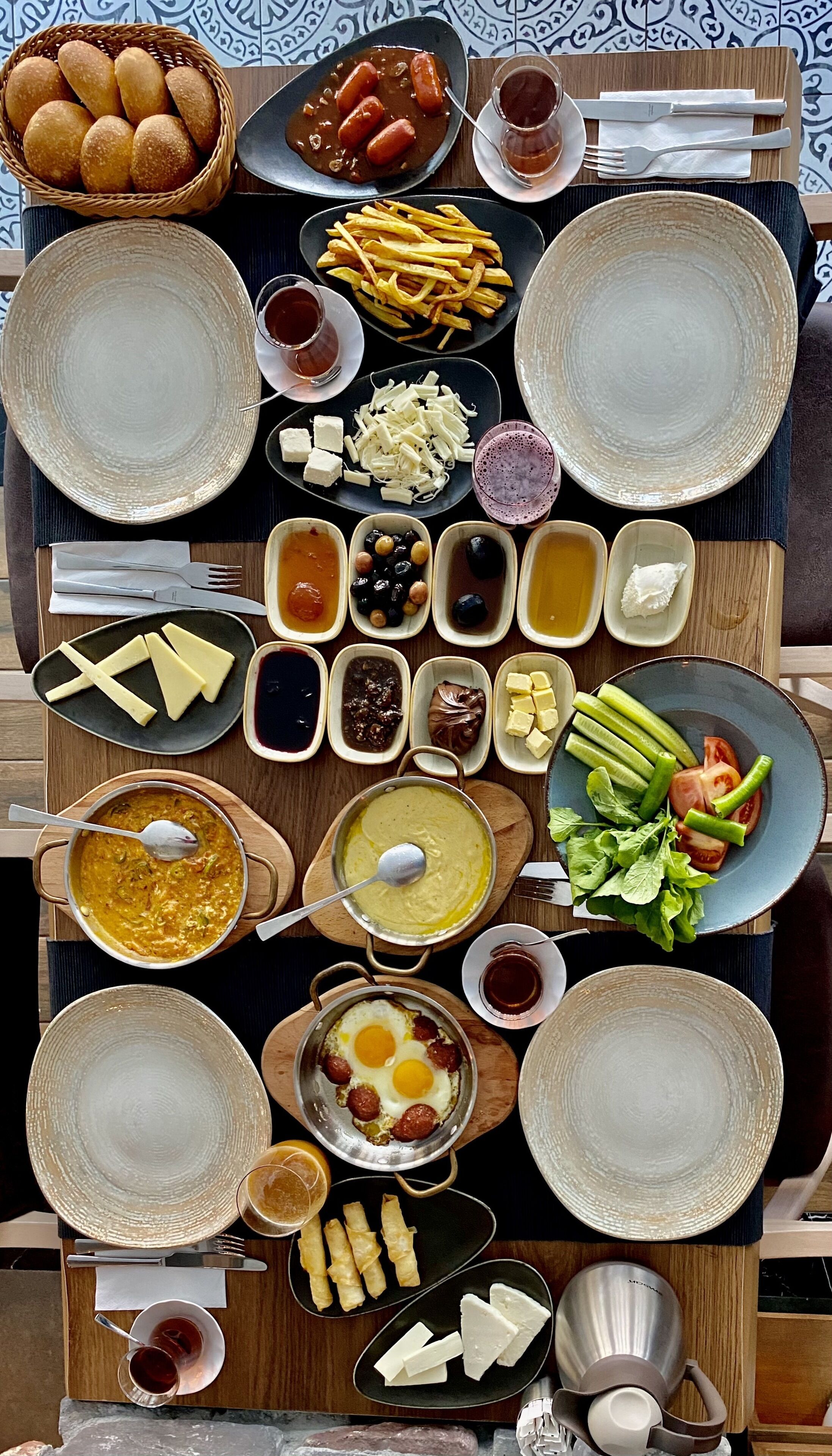 A table set with various dishes including bread, sausages, fries, and salads, suggesting a meal setup.