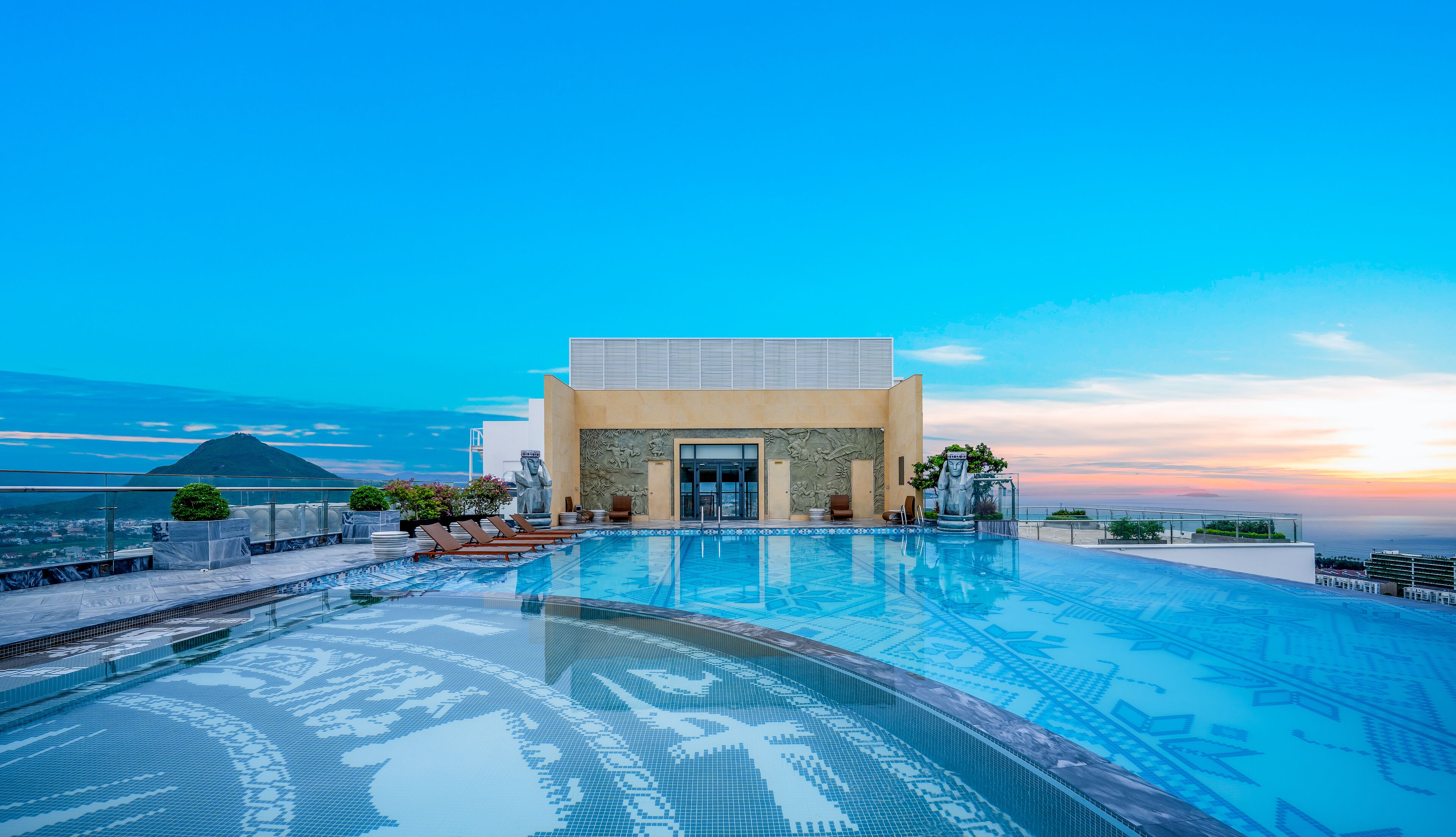 Un hotel moderno con una amplia piscina infinita, vistas a la montaña y una estatua en primer plano.