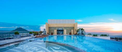 Un hotel moderno con una amplia piscina infinita, vistas a la montaña y una estatua en primer plano.