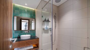 Une salle de bain moderne avec une douche à l’italienne en verre, un meuble-lavabo en bois et un mur orné d’un motif vert.