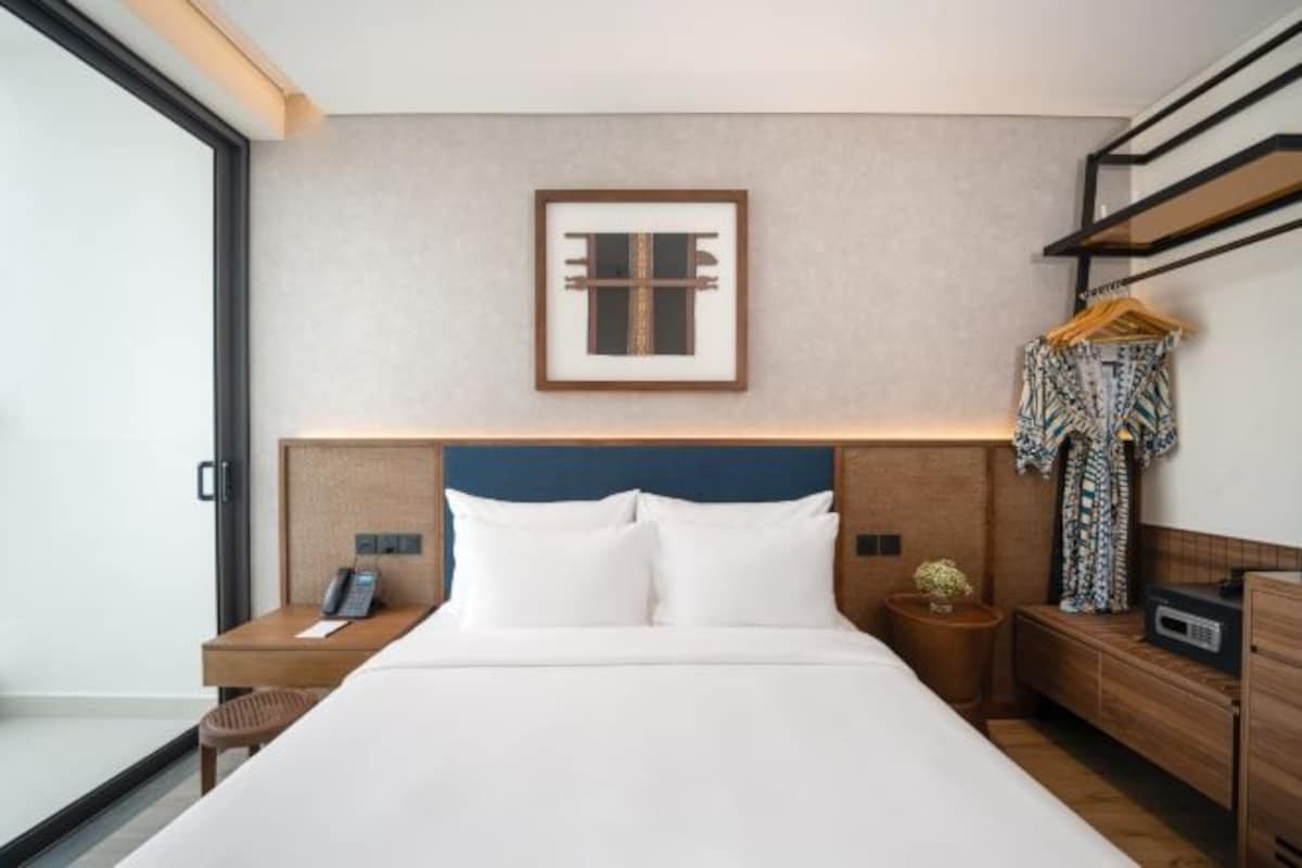 Habitación de hotel con cama, mesitas de noche, teléfono, una obra de arte enmarcada en la pared y un perchero.