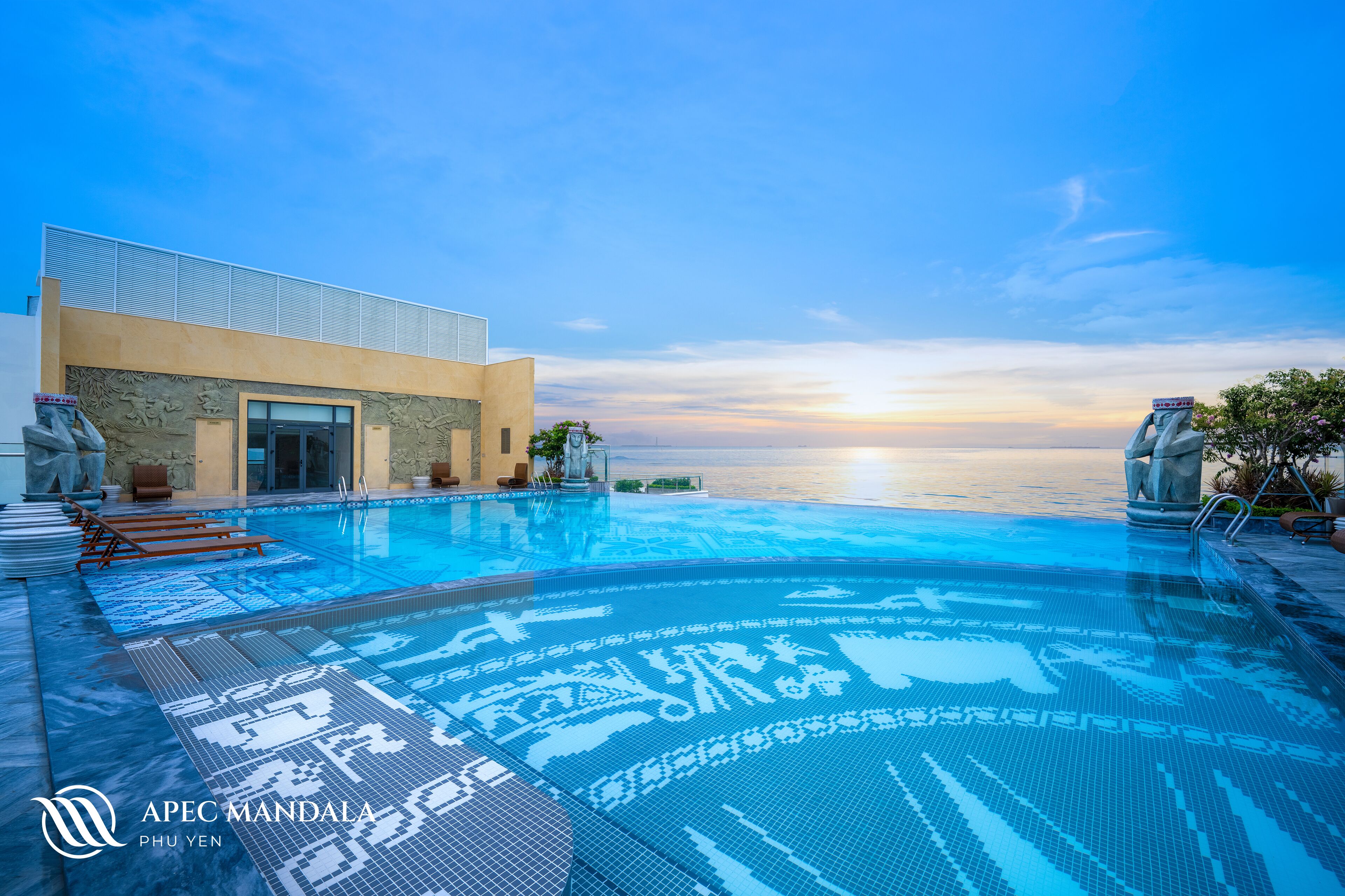 Una piscina con vistas al atardecer, un edificio con fachada de piedra y el logotipo 'APEC MANDALA PHU YEN'.
