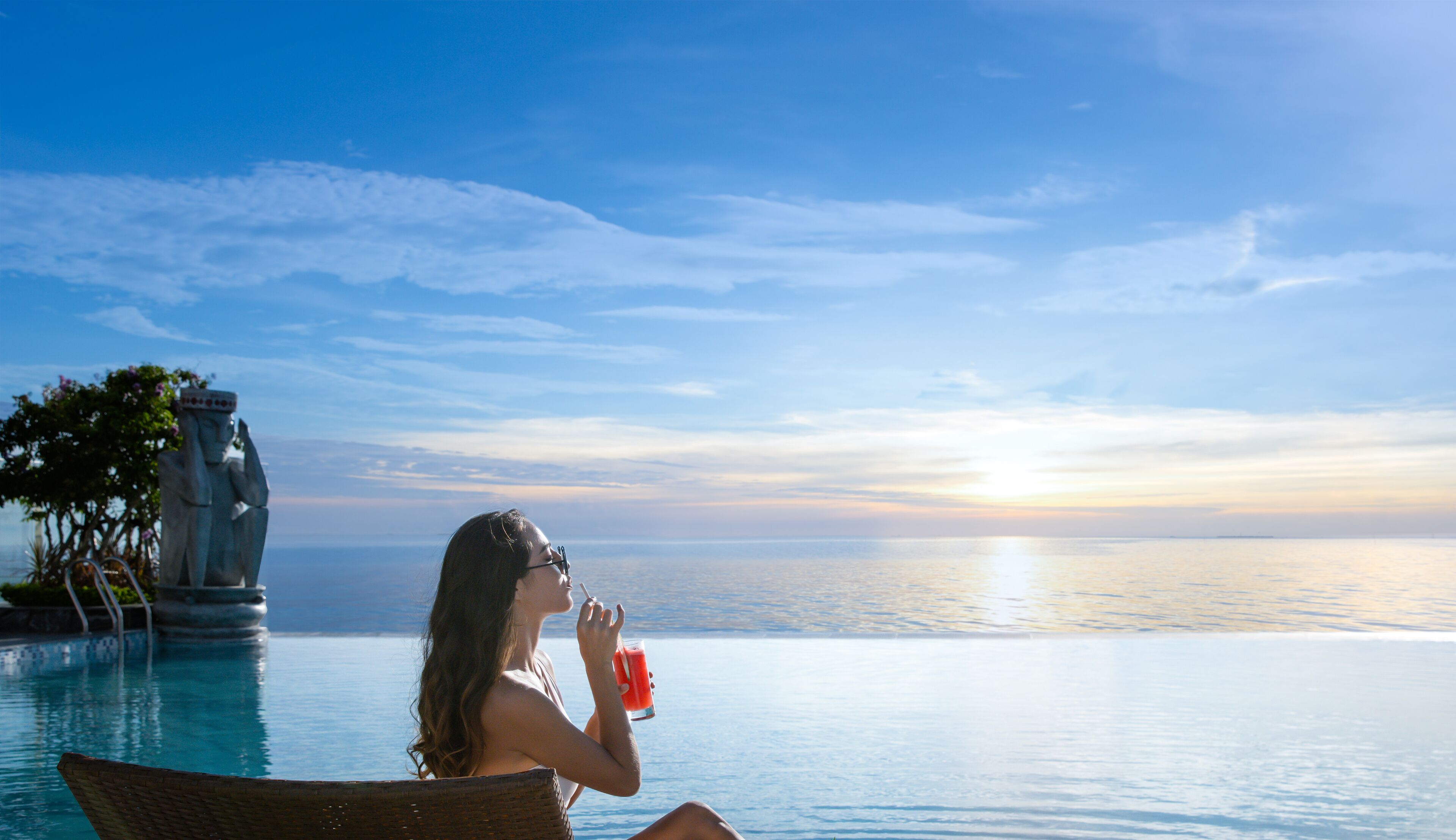 A woman relaxing by a pool with a sunset view.