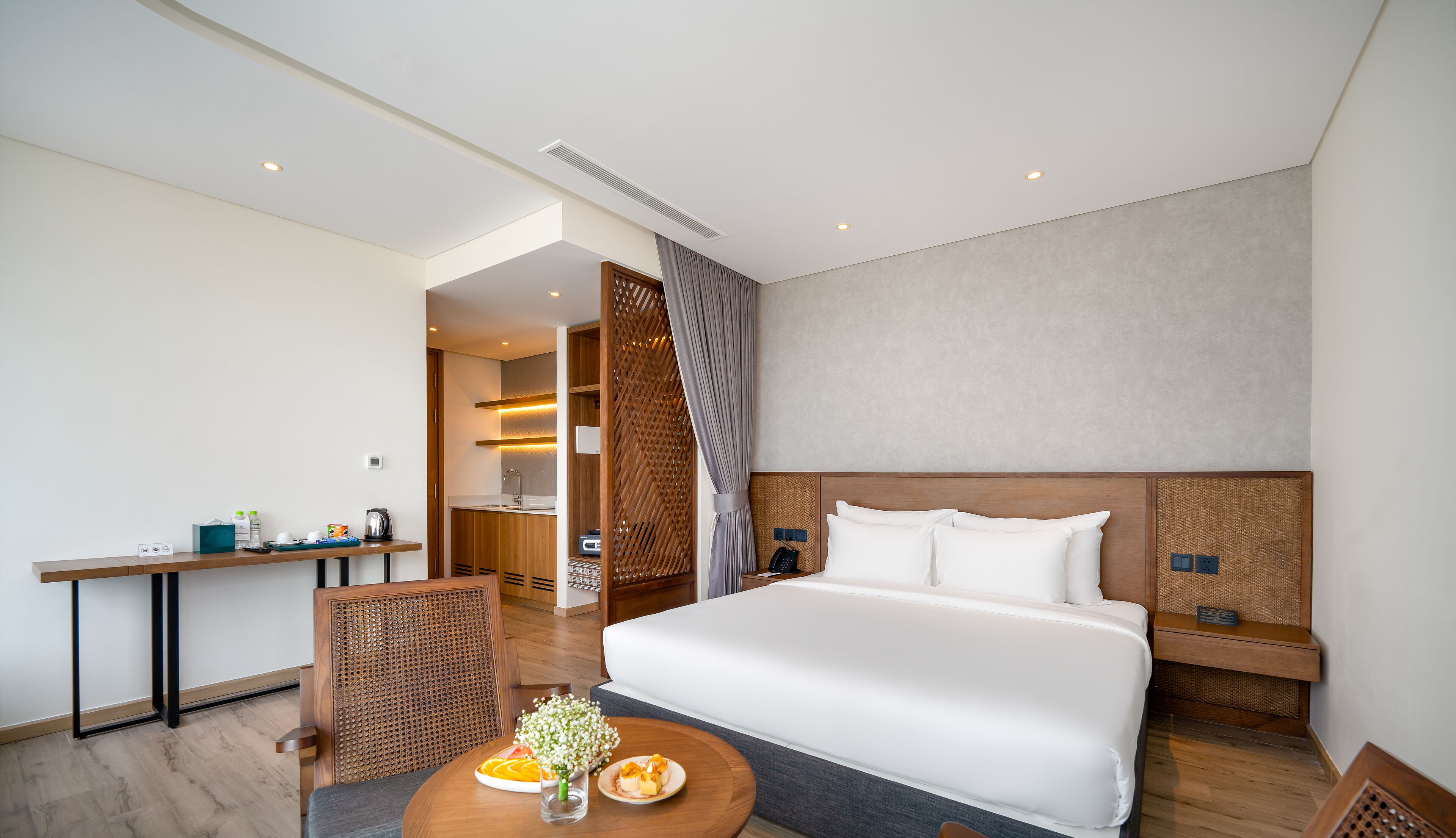 Et moderne hotelværelse med en stor seng, et spisebord med morgenmad, et separat tekøkken og et badeværelse, der ses gennem en dør.