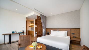 Et moderne hotelværelse med en stor seng, et spisebord med morgenmad, et separat tekøkken og et badeværelse, der ses gennem en dør.
