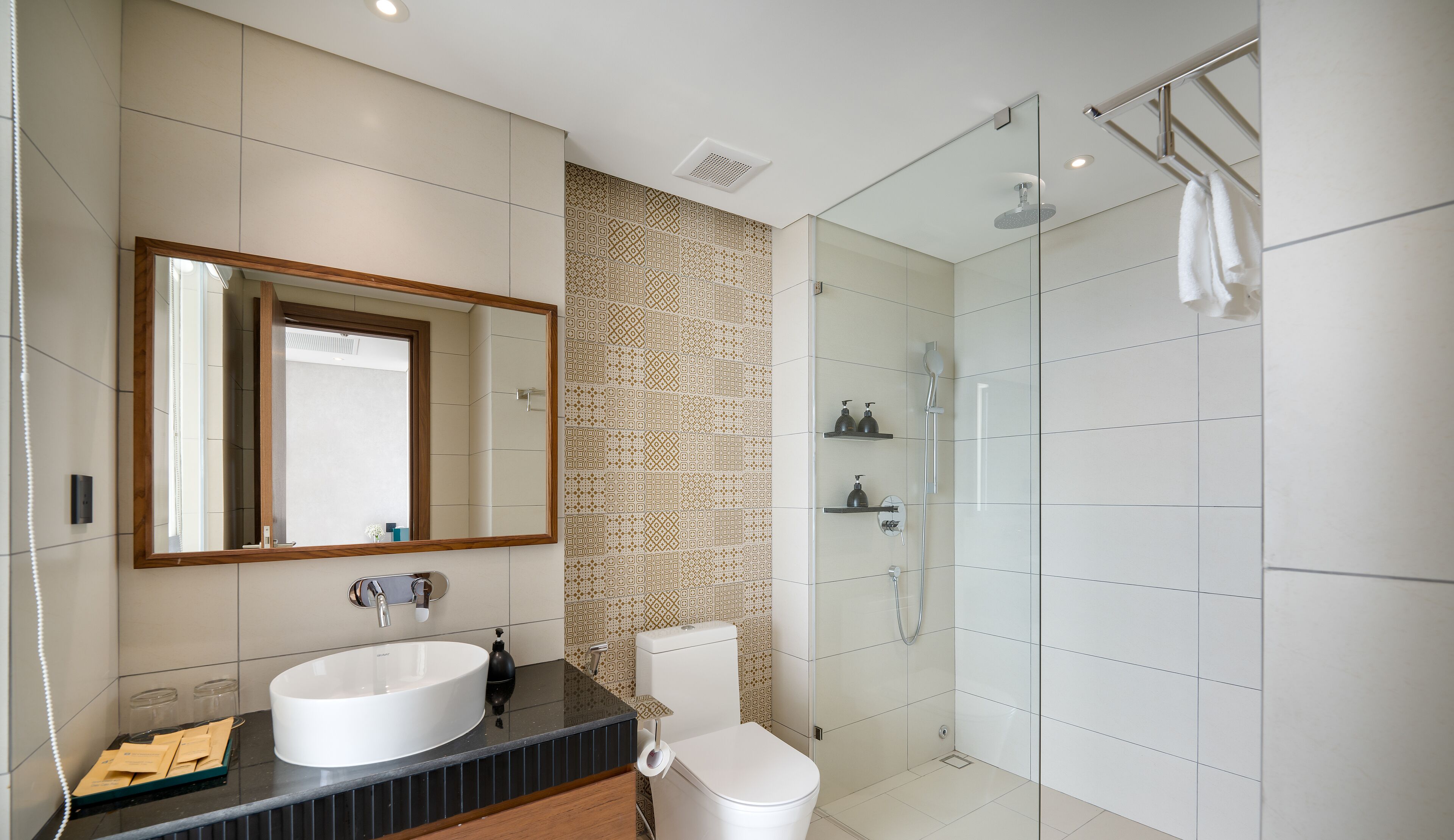 A modern bathroom with a large mirror, a white sink, a toilet, and a glass-enclosed shower area.