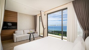 A modern hotel room with a large bed, a sofa, a small table with a vase, and a view of the sea. - Mandala Hotel & Spa Phu Yen - 24-hour stay (Tuy Hoa)