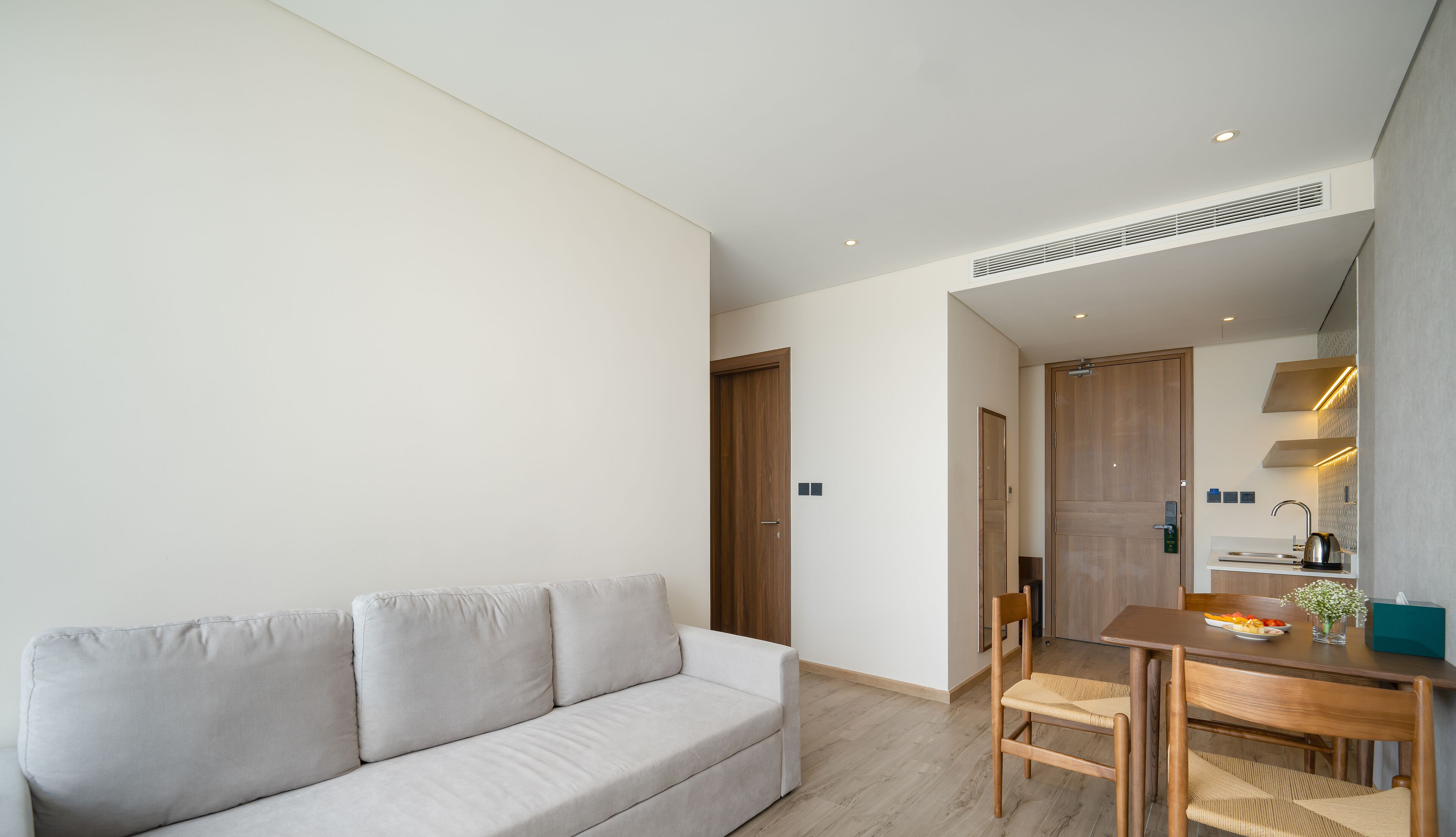 Una sala de estar moderna con un sofá, un comedor con una mesa y sillas, y una cocina visible a través de una puerta abierta.