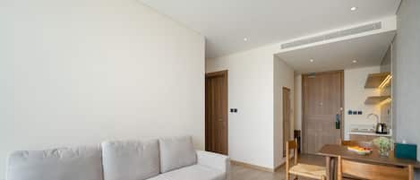 Una sala de estar moderna con un sofá, un comedor con una mesa y sillas, y una cocina visible a través de una puerta abierta.