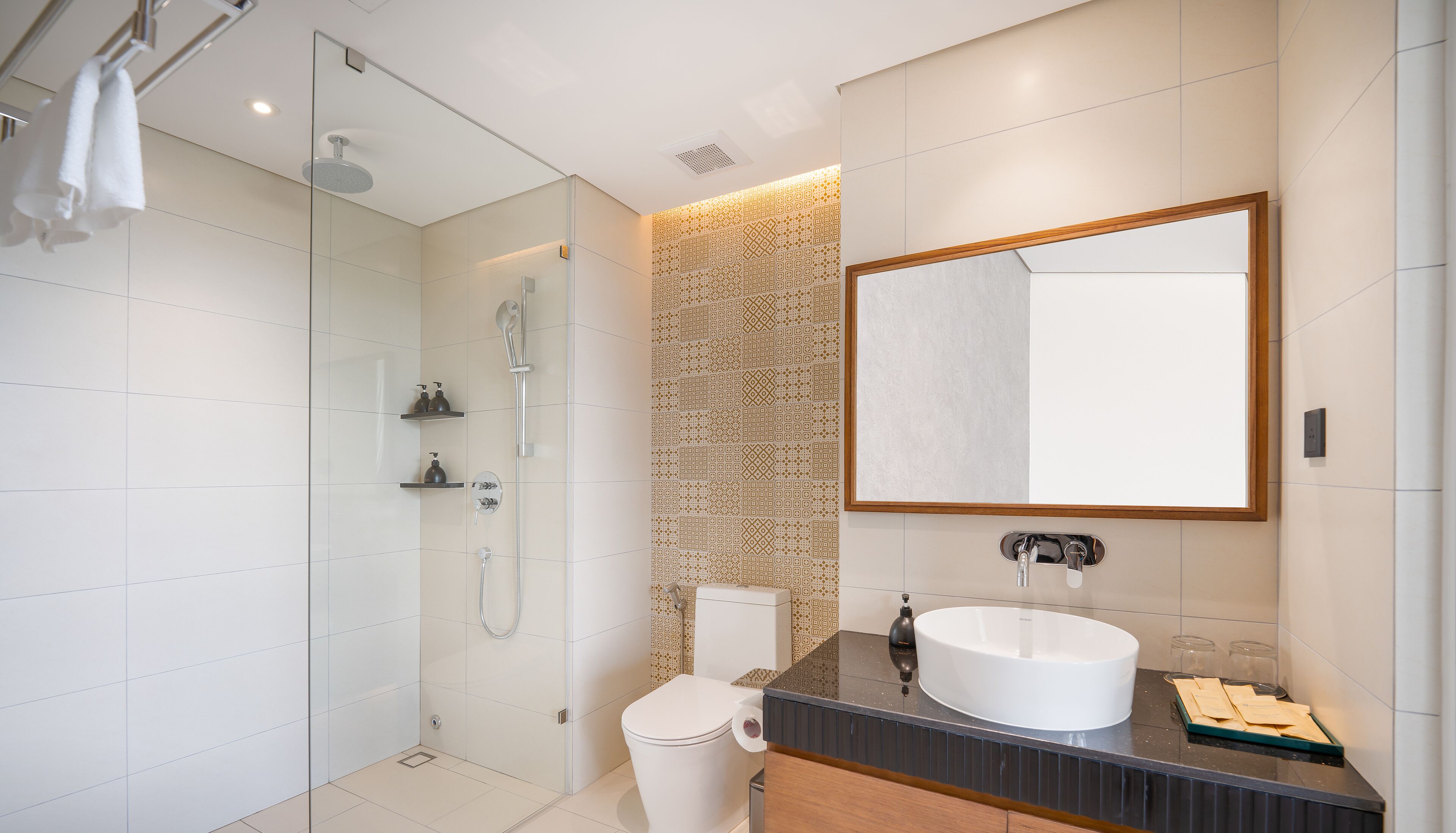 A modern bathroom with a glass-enclosed shower, a toilet, a sink with a mirror, and patterned tiles.