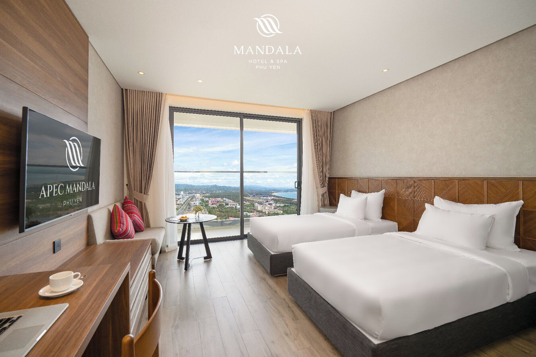 A hotel room with two beds, a TV, a desk with a cup and saucer, and a view of the city.