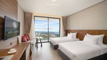 A hotel room with two beds, a TV, a desk with a cup and saucer, and a view of the city.