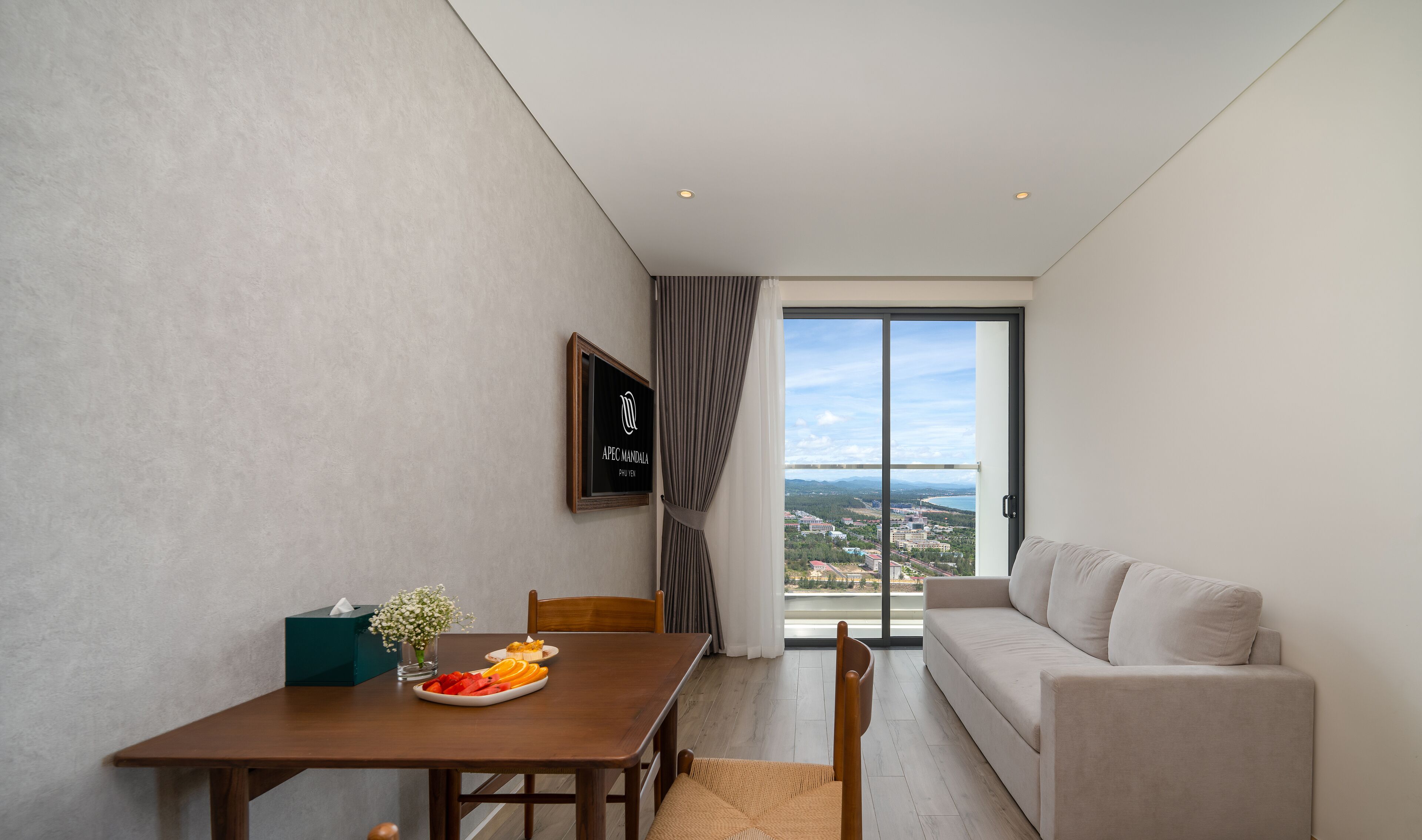 Et moderne hotelværelse med spiseplads, en sofa og et stort vindue med udsigt over byen.
