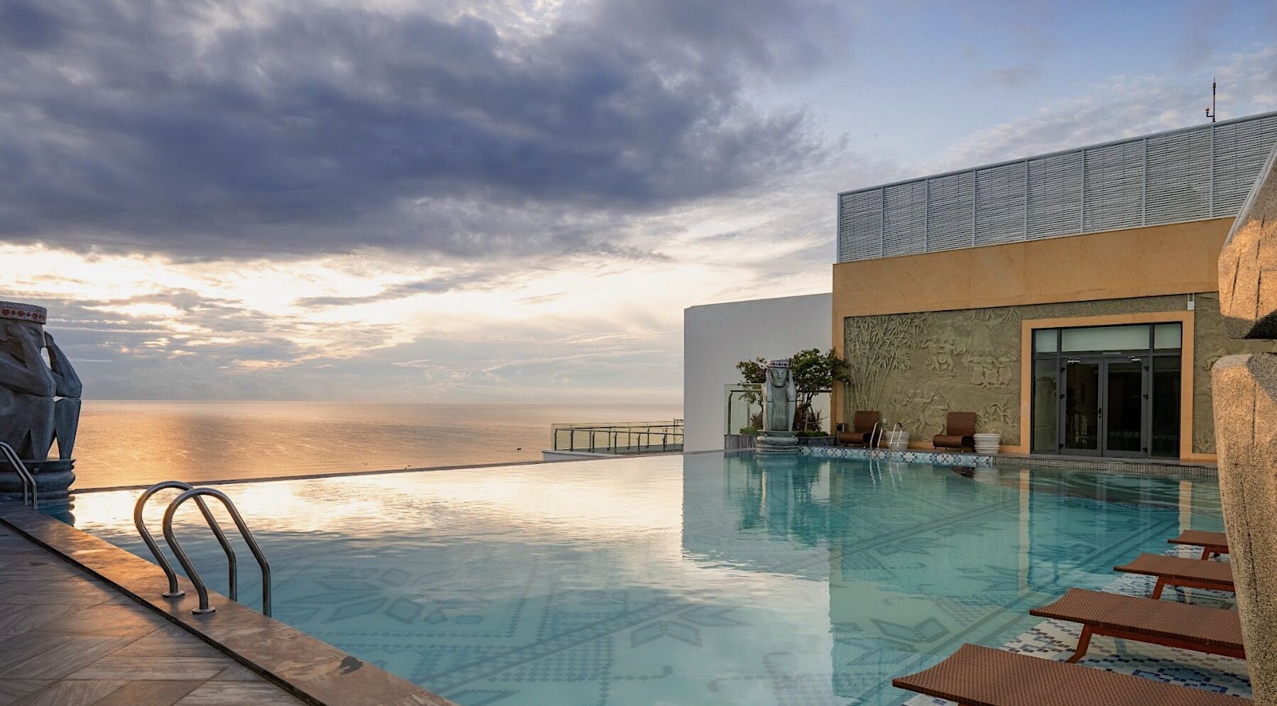 A pool with a view of the ocean, a statue, and a building with a textured facade.