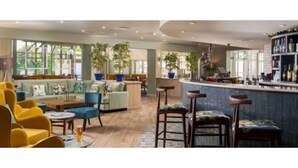 Un espace bar moderne avec un comptoir et des tabourets, un coin salon avec des canapés et des fauteuils, et de grandes fenêtres qui laissent entrer la lumière naturelle.