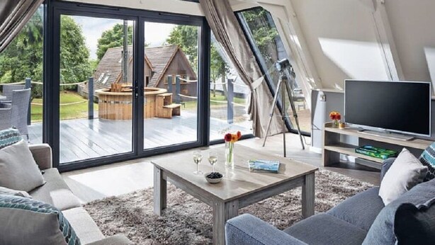 Un salon moderne doté d’une grande porte-fenêtre coulissante donnant sur une terrasse, d’un téléviseur à écran plat et d’un coin salon confortable.