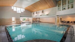 Une grande piscine intérieure à eau claire, entourée d’un sol carrelé et dotée de plusieurs points d’accès.