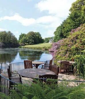 Eine Uferterrasse mit Holztischen und -stühlen, umgeben von üppiger Vegetation und Blick auf den Fluss.