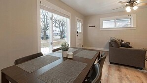 Ein Essbereich mit Tisch, Stühlen, Deckenventilator und Fenster mit Blick auf Bäume und parkende Autos.
