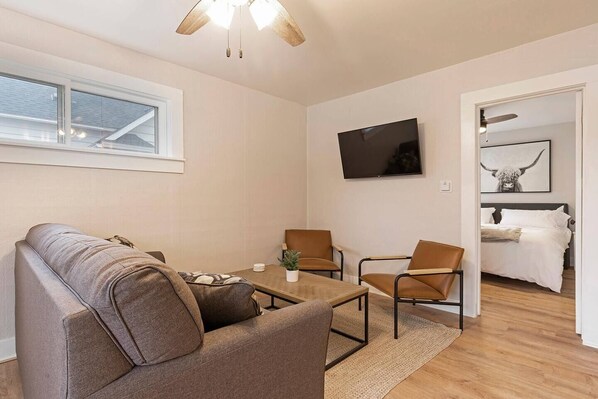 A modern living room with a sofa, two armchairs, a coffee table, and a TV. There is a window and a door leading to a bedroom. - Slant Streets Bungalow - Close proximity to The Hip Strip, Downtown Missoula and UM. (Missoula)