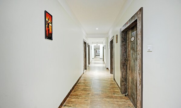 A long, narrow hallway with white walls and a wooden floor. There are doors on both sides, some with numbers on them.