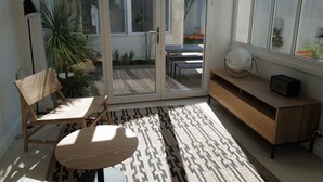 A modern room with a sliding glass door leading to a patio, a wooden chair, a small round table, a patterned rug, and a wooden console table with a speaker. - Very nice 4* listed Rhétaise house with garden and garage, quiet, right in the center, (Le Bois-Plage-en-Re)