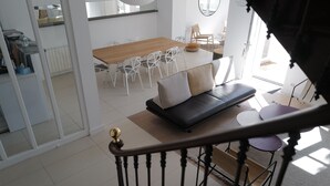 A modern living room with a sofa, a dining table with chairs, and a staircase. - Very nice 4* listed Rhétaise house with garden and garage, quiet, right in the center, (Le Bois-Plage-en-Re)