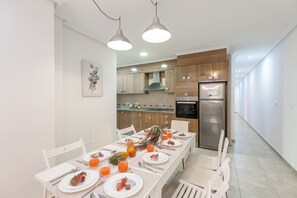 Een moderne keuken met houten kastjes, een roestvrijstalen koelkast en een ontbijtgedeekte eettafel met witte stoelen.