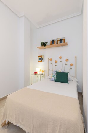 Ein ordentlich eingerichtetes Schlafzimmer mit einem Bett, Nachttischen und einer an der Wand befestigten Ablage mit Dekoration.