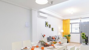 Comedor con una mesa blanca dispuesta para cuatro personas, sillas e iluminación colgante.