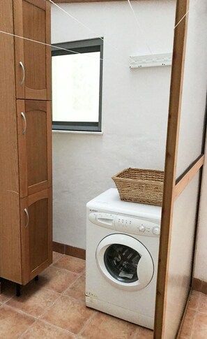 Ein Waschraum mit Waschmaschine, Holzschrank und Fenster.