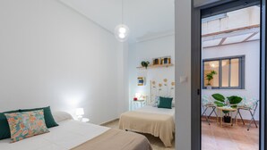 A hotel room with two beds, a small table with a lamp, a potted plant, and a sliding door to an outdoor area. - Enjoy life in our apartment. Wifi & Parking (Guardamar)