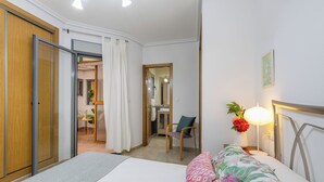 Habitación de hotel con cama, una silla, escritorio y baño visible a través de una puerta abierta.