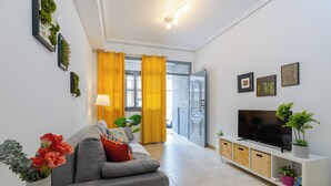 Una sala moderna con un sofá gris, un televisor sobre un mueble blanco y una planta en el mueble.