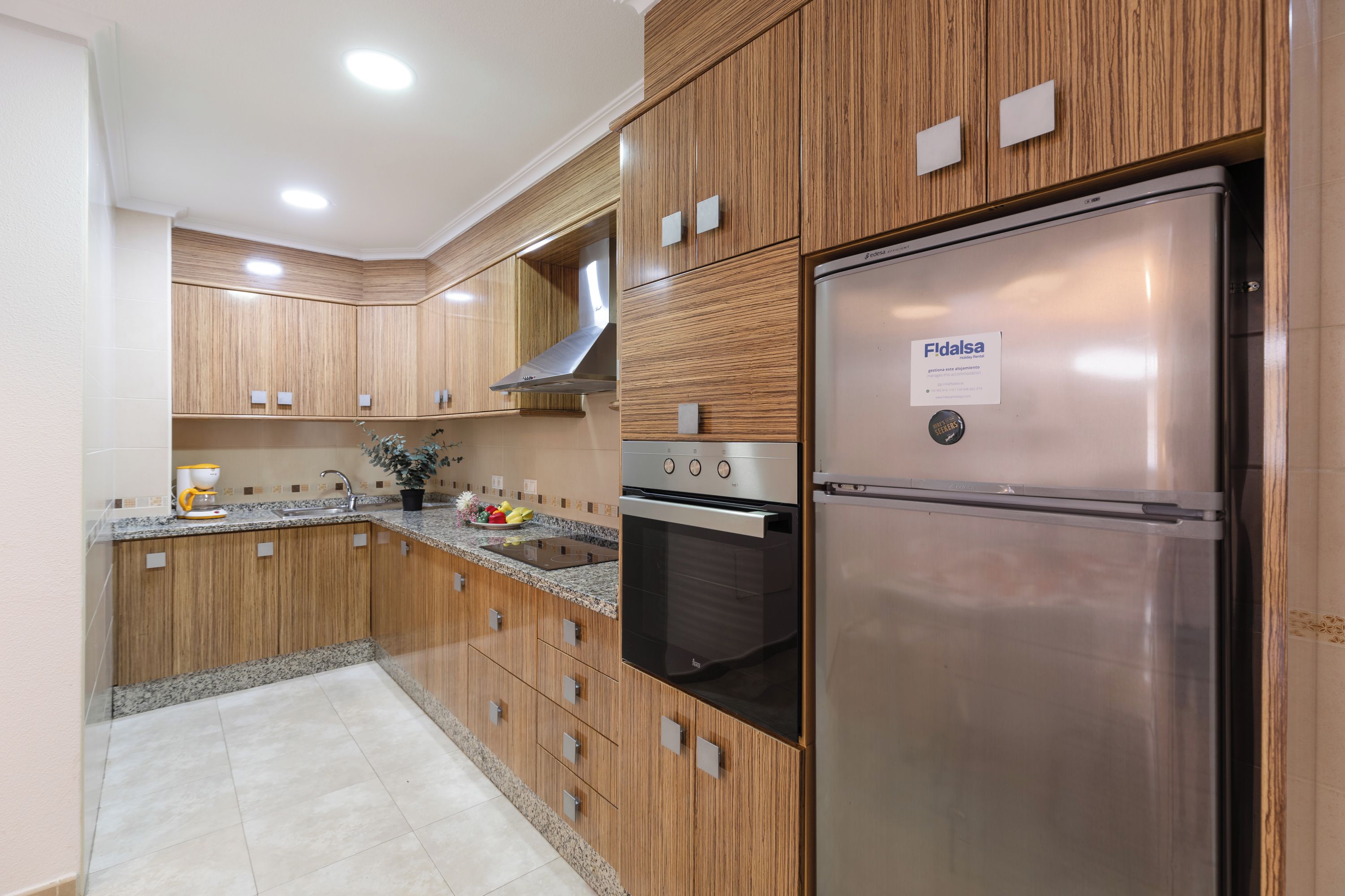 A modern kitchen with wooden cabinets, a stainless steel refrigerator, and a built-in oven.